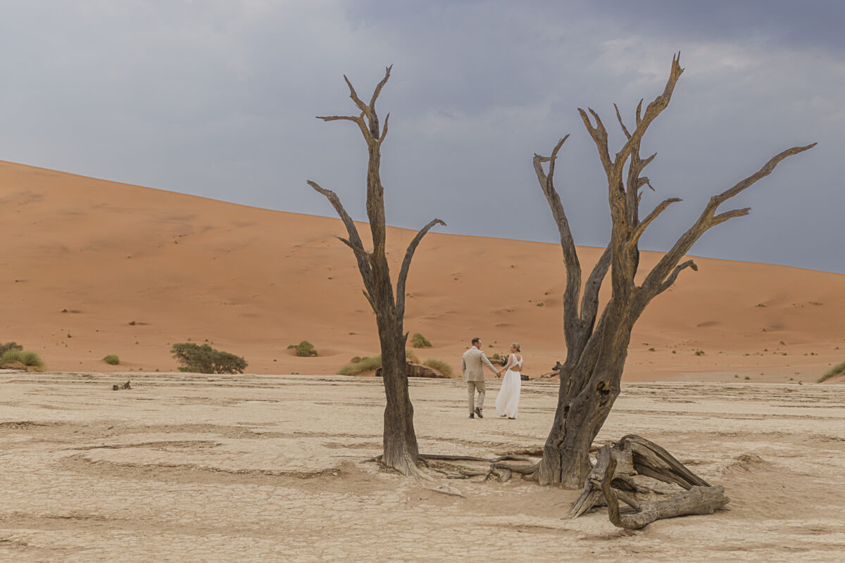 Couple standing in Deadvlei, framed by ancient camel thorn trees and soft desert hues, photographed on their Namibian honeymoon, image by Mariette du Toit Photography