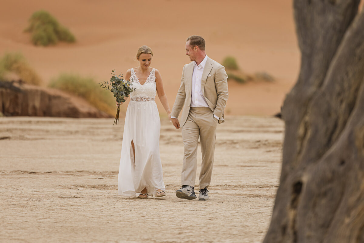 Bride and groom walking hand in hand across the white clay pan of Sossusvlei during their wedding photoshoot, image by Mariette du Toit Photography