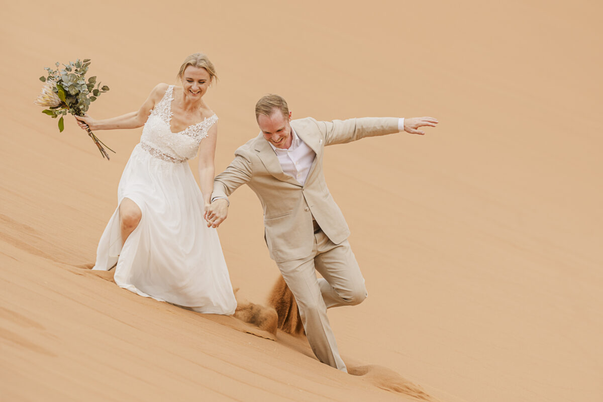 couple playing in Sossusvlei dunes during wedding photo shoot, image by Mariette du Toit Photography