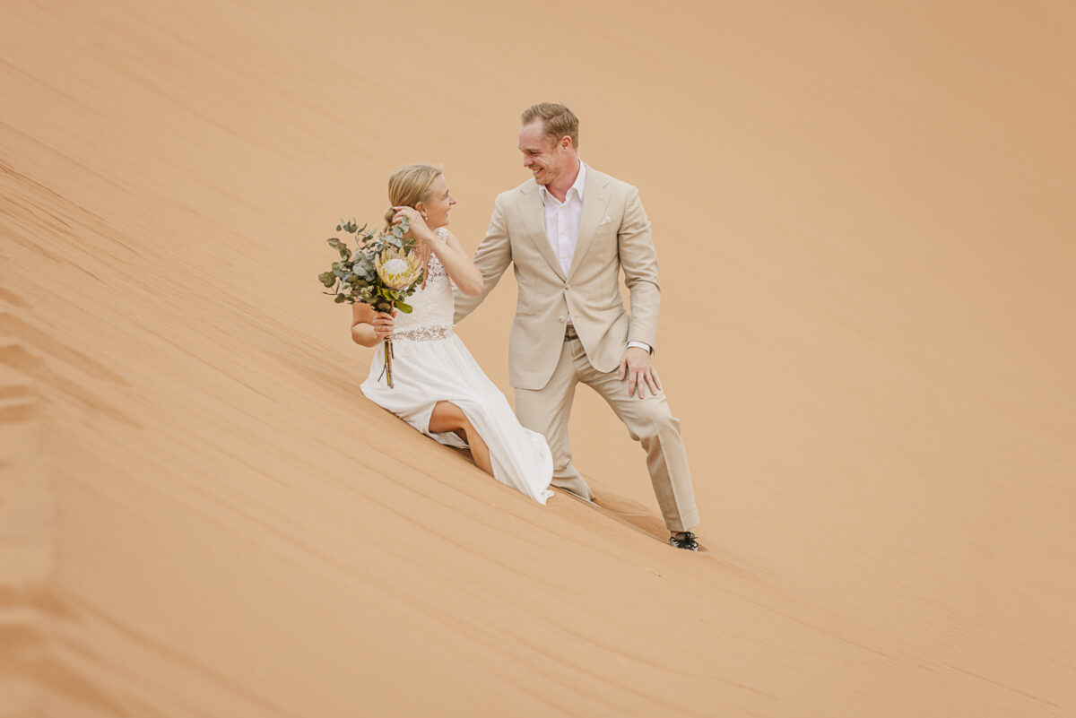 couple playing in Sossusvlei dunes during wedding photo shoot, image by Mariette du Toit Photography
