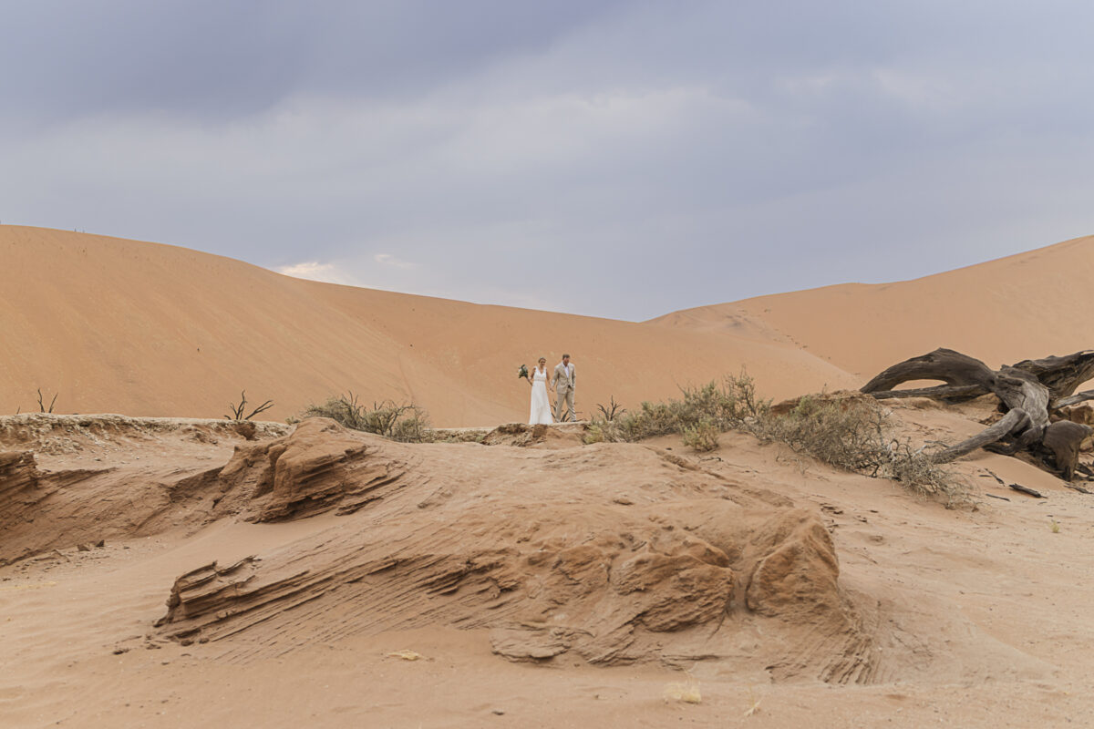 Bride and groom walking hand in hand across dunes of Sossusvlei during their wedding photoshoot, image by Mariette du Toit Photography
