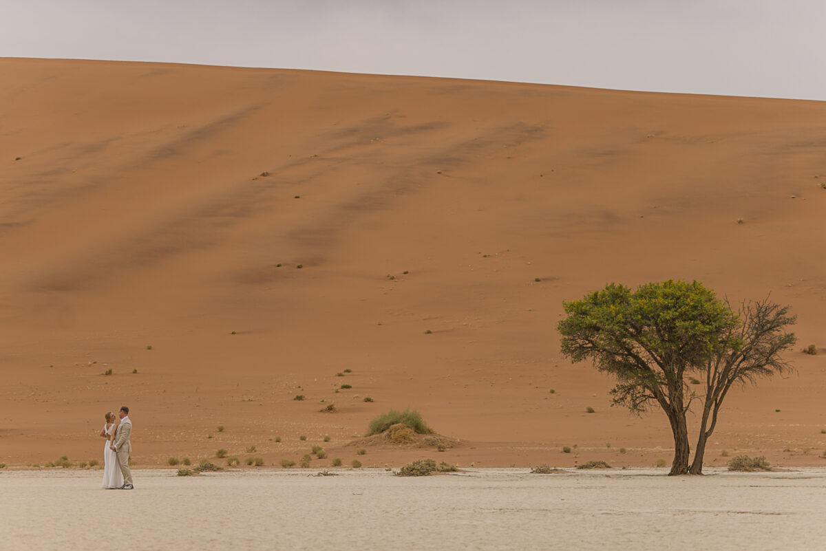 Dancing couple against the muted tones of the Namib Desert dunes on an overcast day, image by Mariette du toit Photography