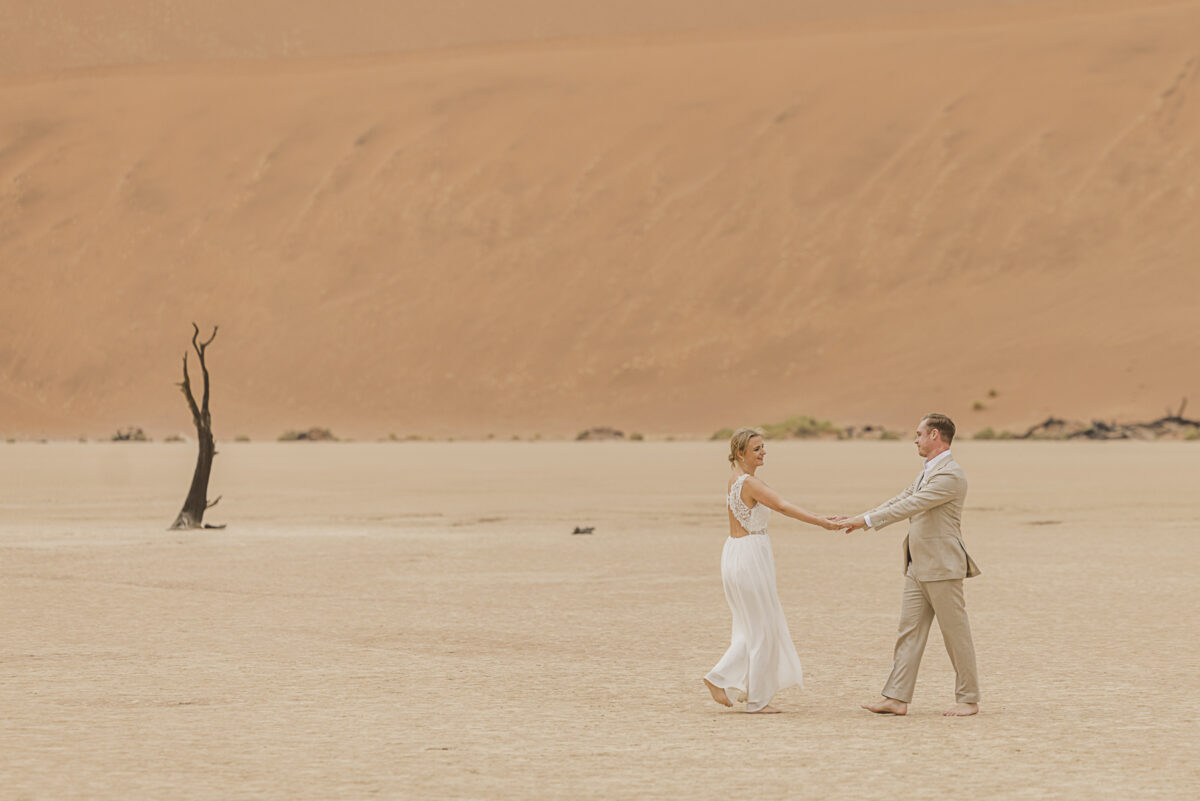 Bride and groom walking hand in hand across the white clay pan of Sossusvlei during their wedding photoshoot, image by Mariette du Toit Photography