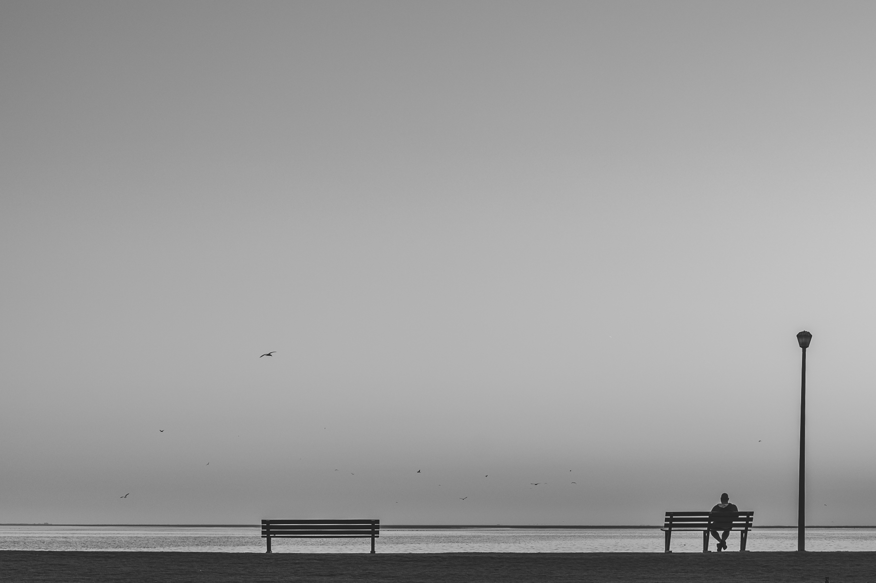 Black and white image of a man sitting on a bench in Walvis Bay, photo by Mariette du Toit.