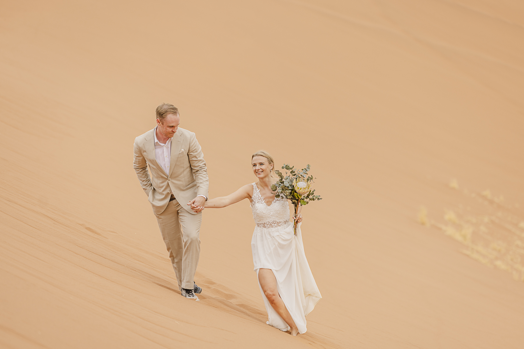 couple walking hand-in-hand in dunes at sossusvlei, namibia during elopement