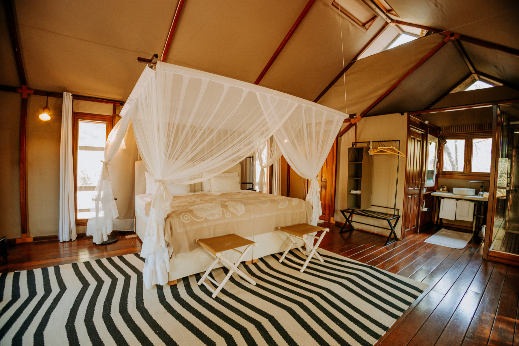 Tented room at Mushara Outpost with a four-poster bed, white mosquito net and zebra-stripe rug