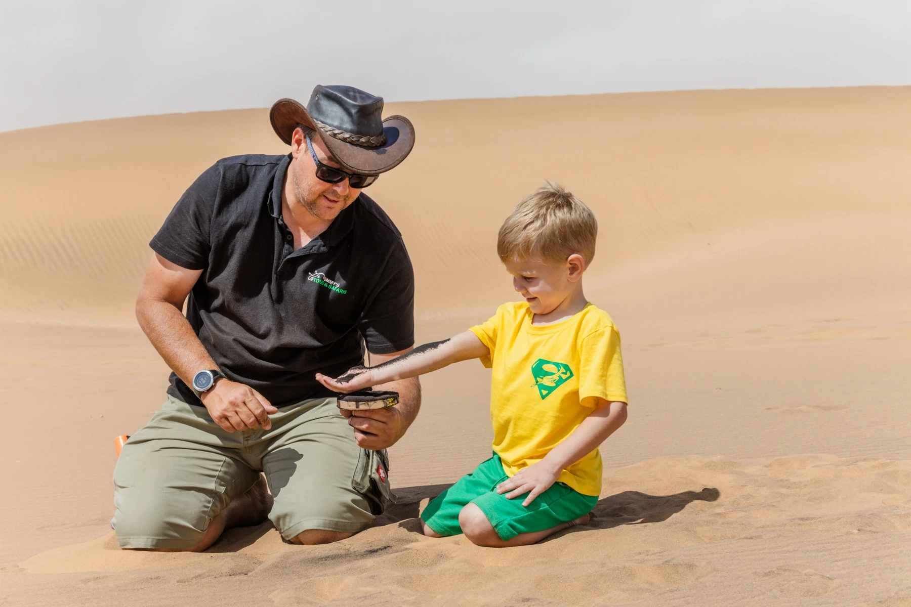Tommy's Living Desert Tours guide showing a young boy a small desert creature in the dunes near Swakopmund