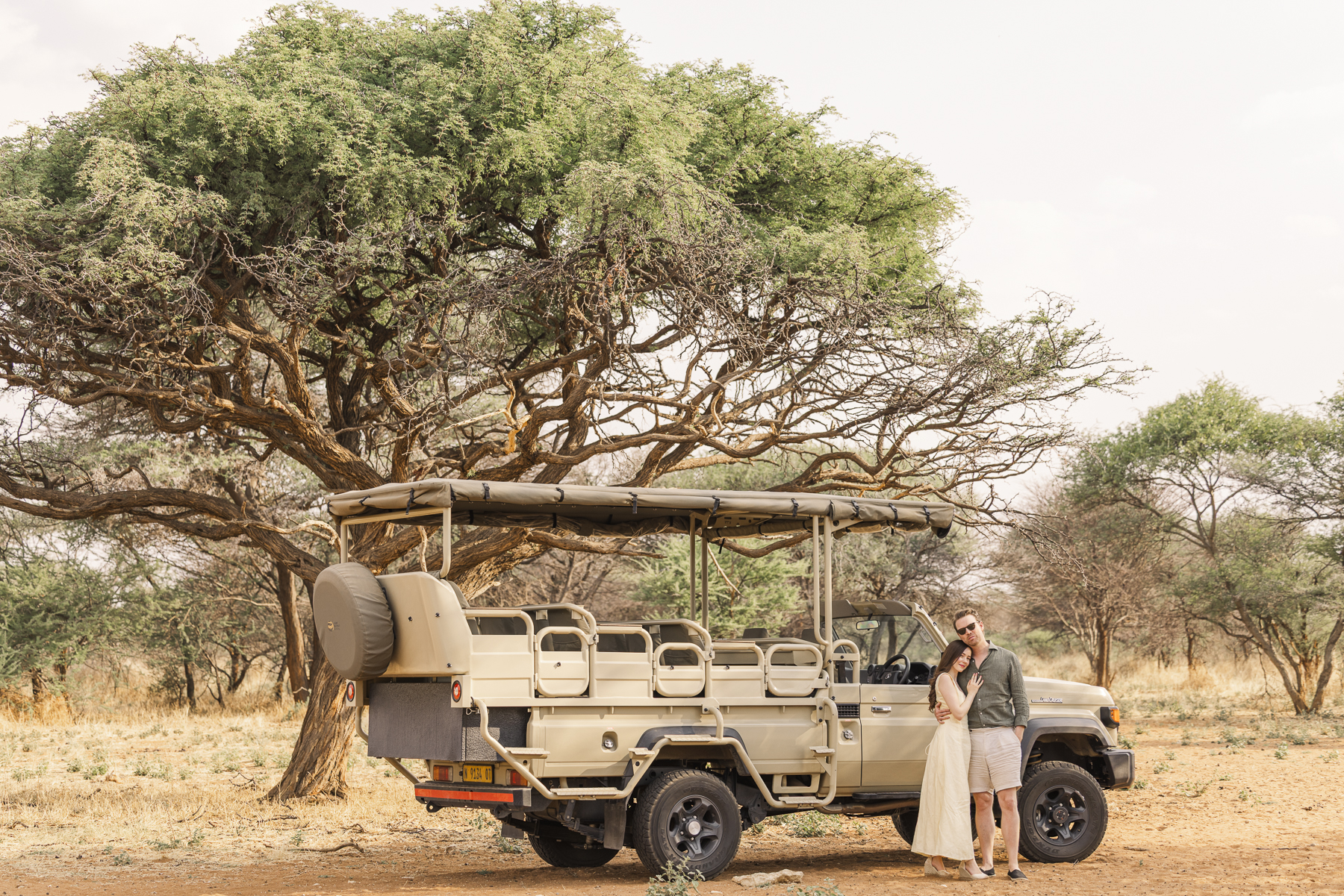 Couple beside a safari vehicle under an acacia tree at Frans Indongo Lodge
